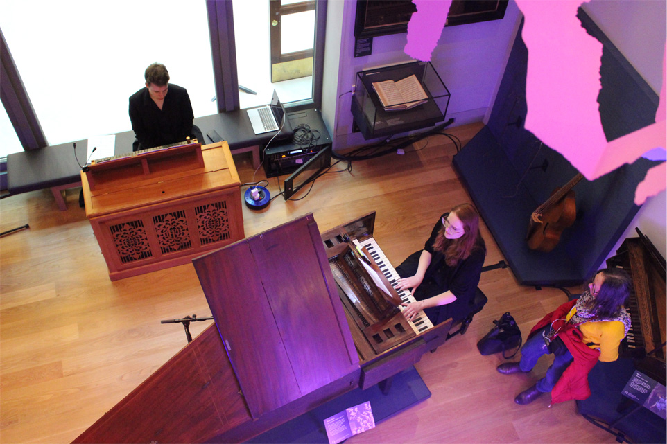 A male and female students, of the Royal College of Music, perform on a harpsichord and an organ in the Museum gallery while visitors explore the gallery.